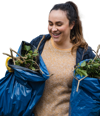 A woman carrying two blue rubbish bags full of garden waste smiling and looking happy