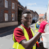A young man outside painting a wall on a street wearing a reflective vest