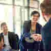 A woman leaning over a desk in a business meeting to shake a colleague's hand 