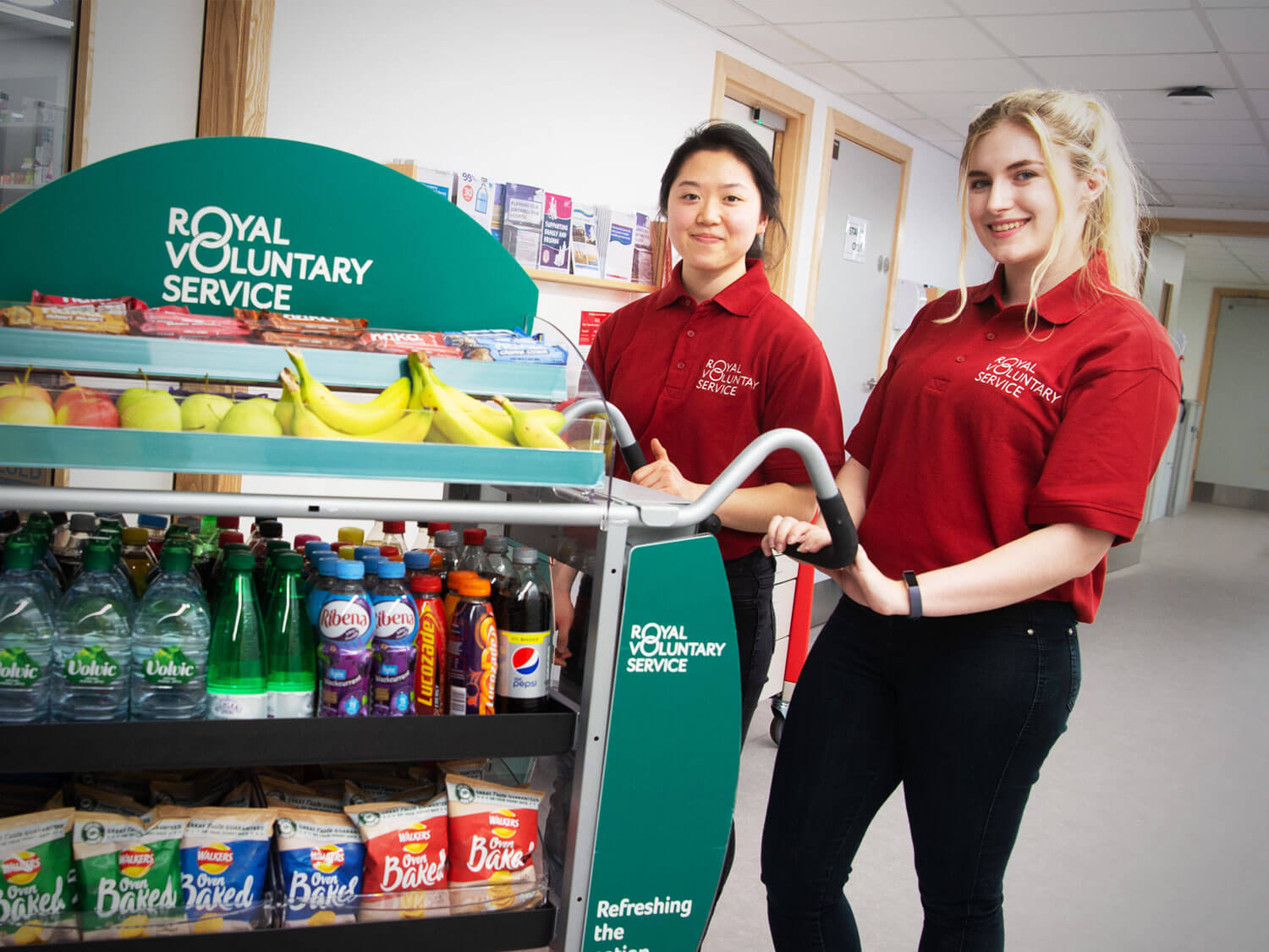 Two young hospital trolley volunteers pushing a Royal Voluntary Service trolley in a hospital ward