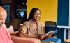 A young woman sat in a business environment smiling and happy whilst using a tablet
