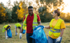 Two young people collecting litter outdoors both wearing gloves and reflective vests