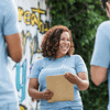 A female volunteer wearing a light blue T-shirt, smiling and looking happy with a clipboard
