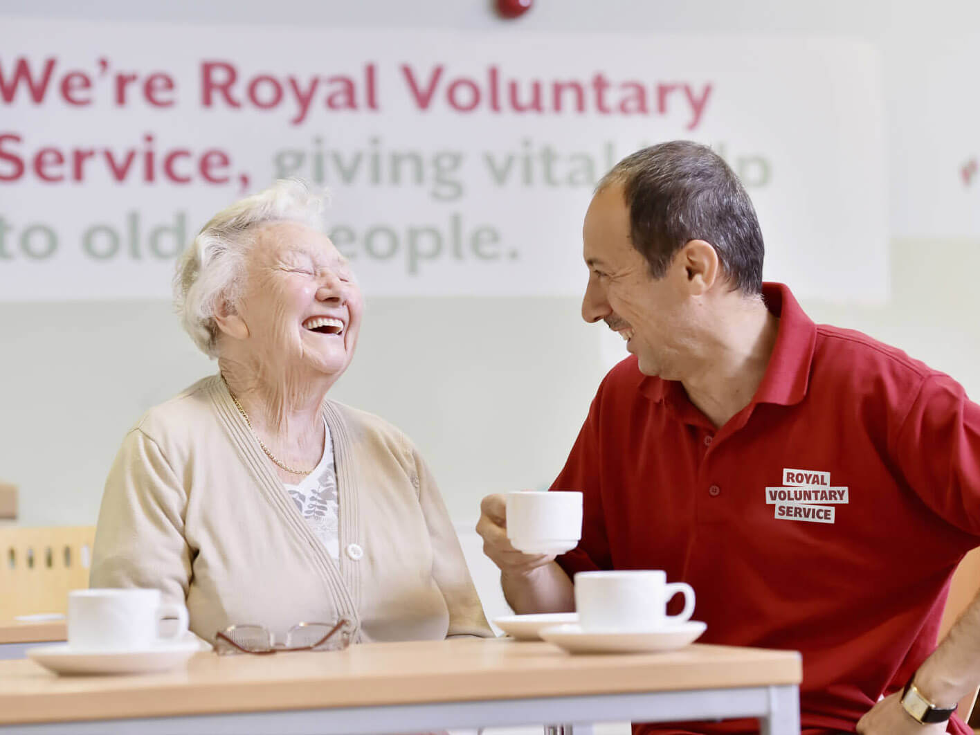 An RVS volunteer making an older lady laugh whilst enjoying a cup of team 